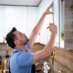 Man carefully measures cabinet heights in a contemporary kitchen during a DIY renovation