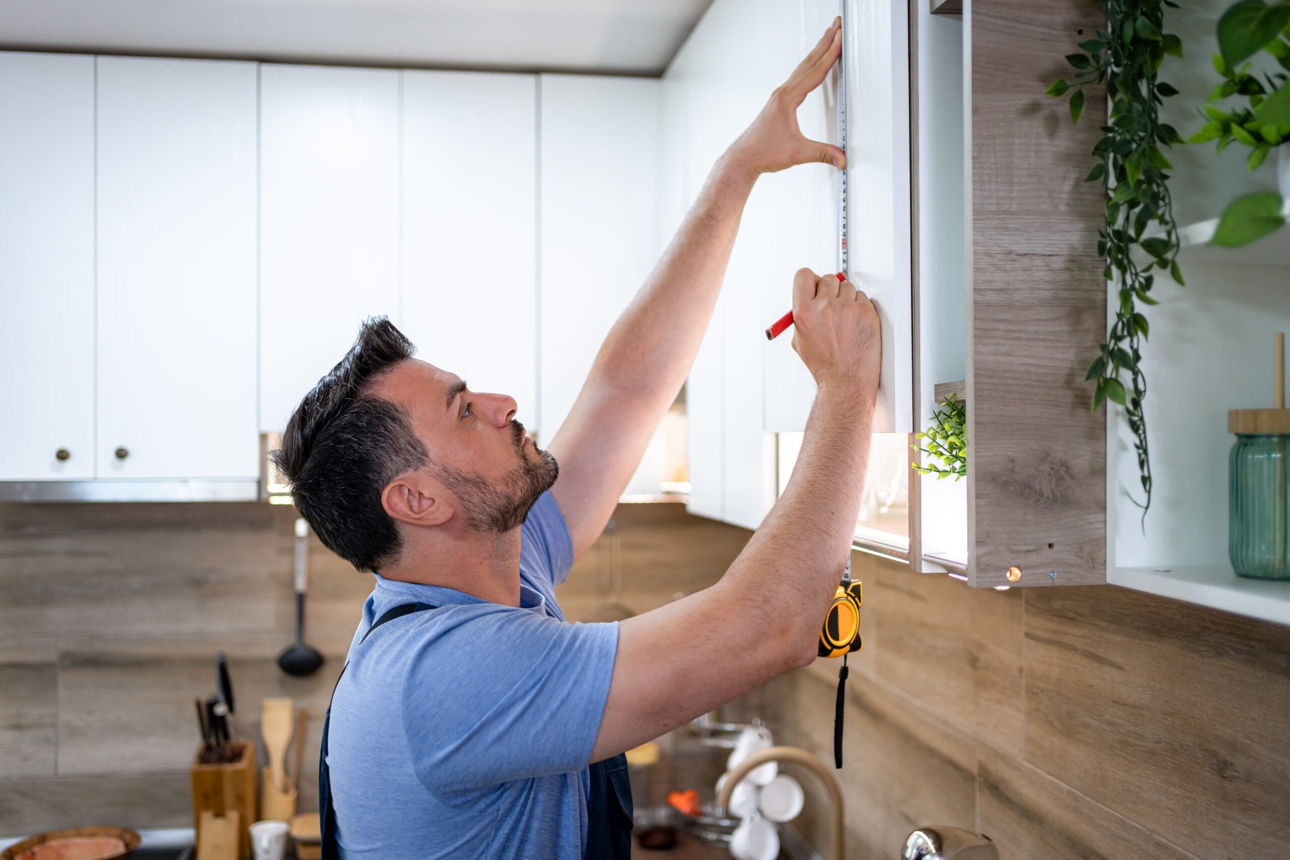 Man carefully measures cabinet heights in a contemporary kitchen during a DIY renovation